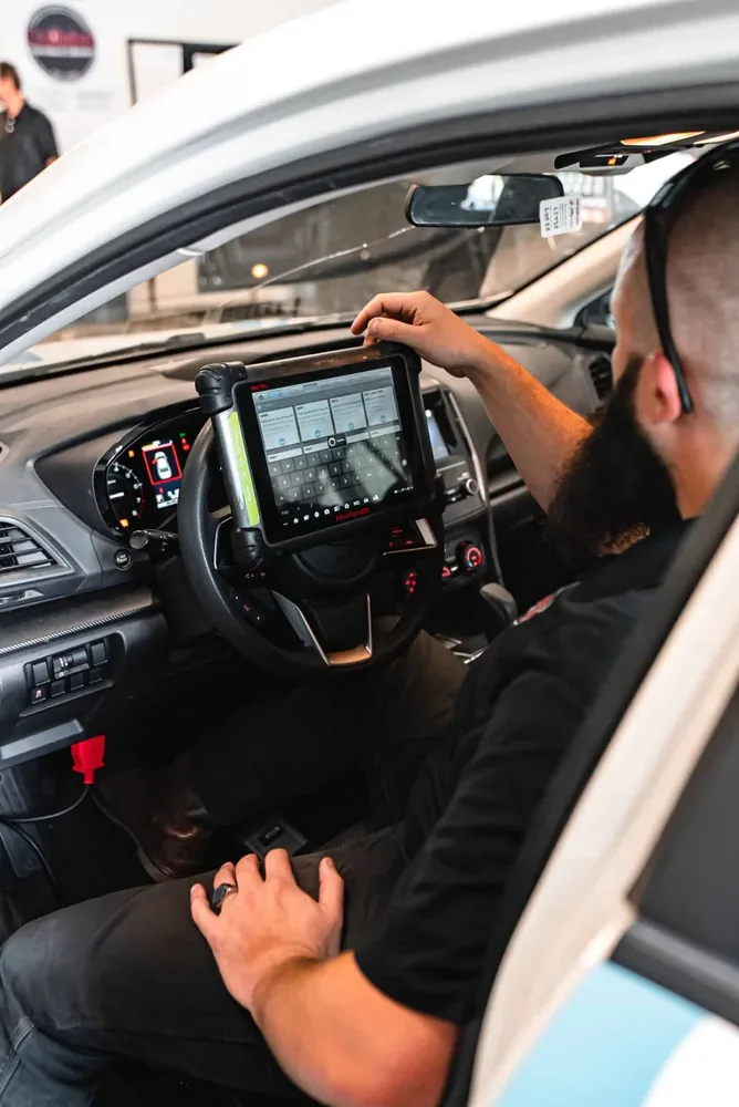 A technician operating a calibration tablet plugged into a vehicle at the dashboard