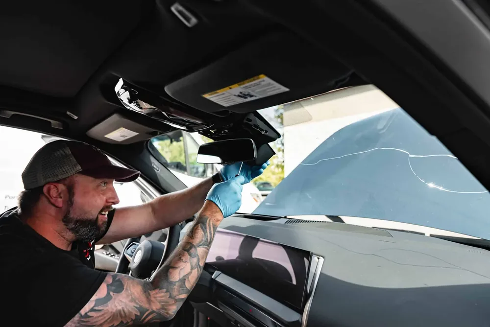 A technician reaching up to the top of the windshield from inside the vehicle cabin