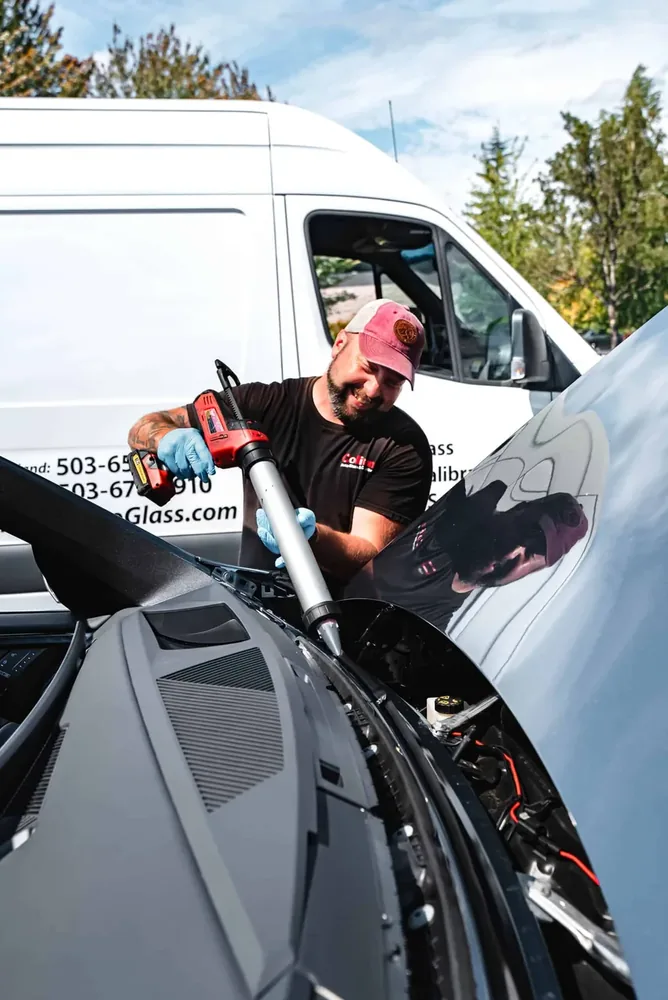 A technician working at the base of the windshield where the wiper cowl meets the glass