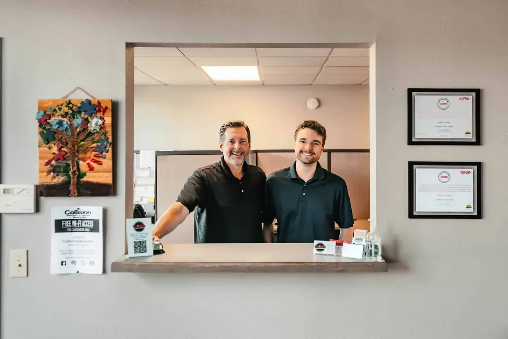 Two staff at the front counter of the shop with framed certificates on the wall behind