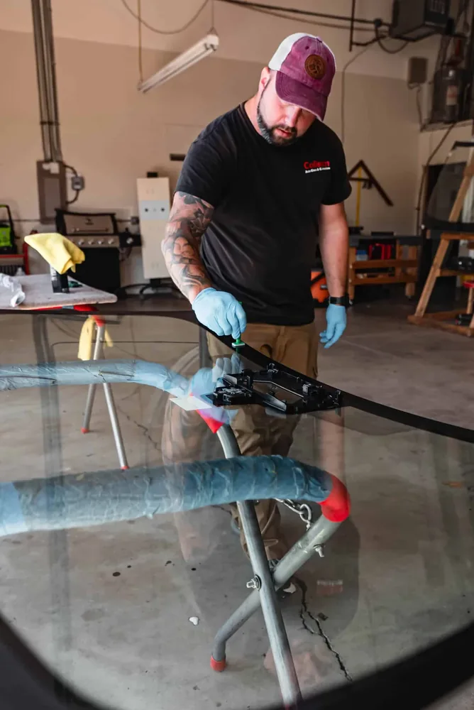 A technician priming the edge of a windshield on a glass stand inside the shop