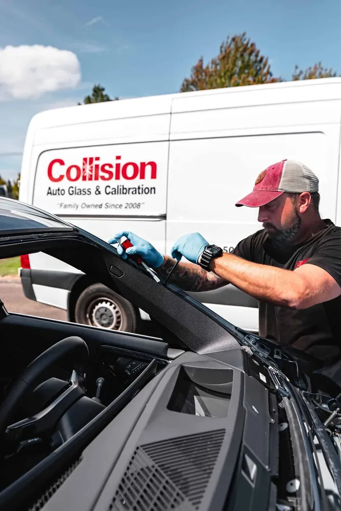A technician setting glass on a car parked beside the branded mobile van