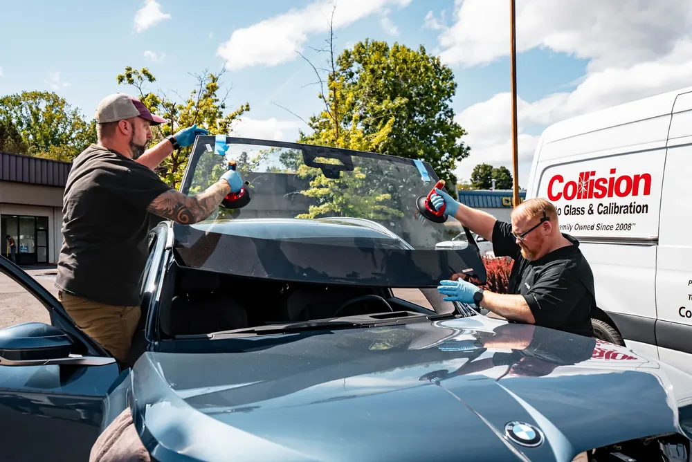 Two technicians lowering a windshield onto a car with suction cup setting tools
